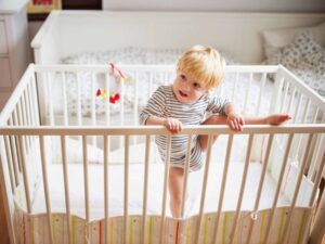 toddler climbing out of crib, ready for toddler bed.